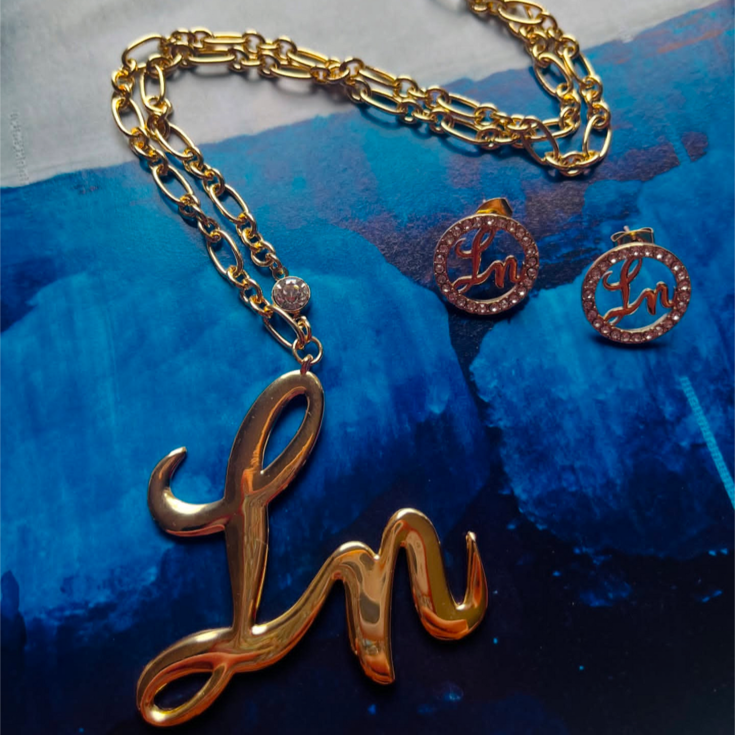 Gold necklace with 'Ln' pendant on a blue textured background