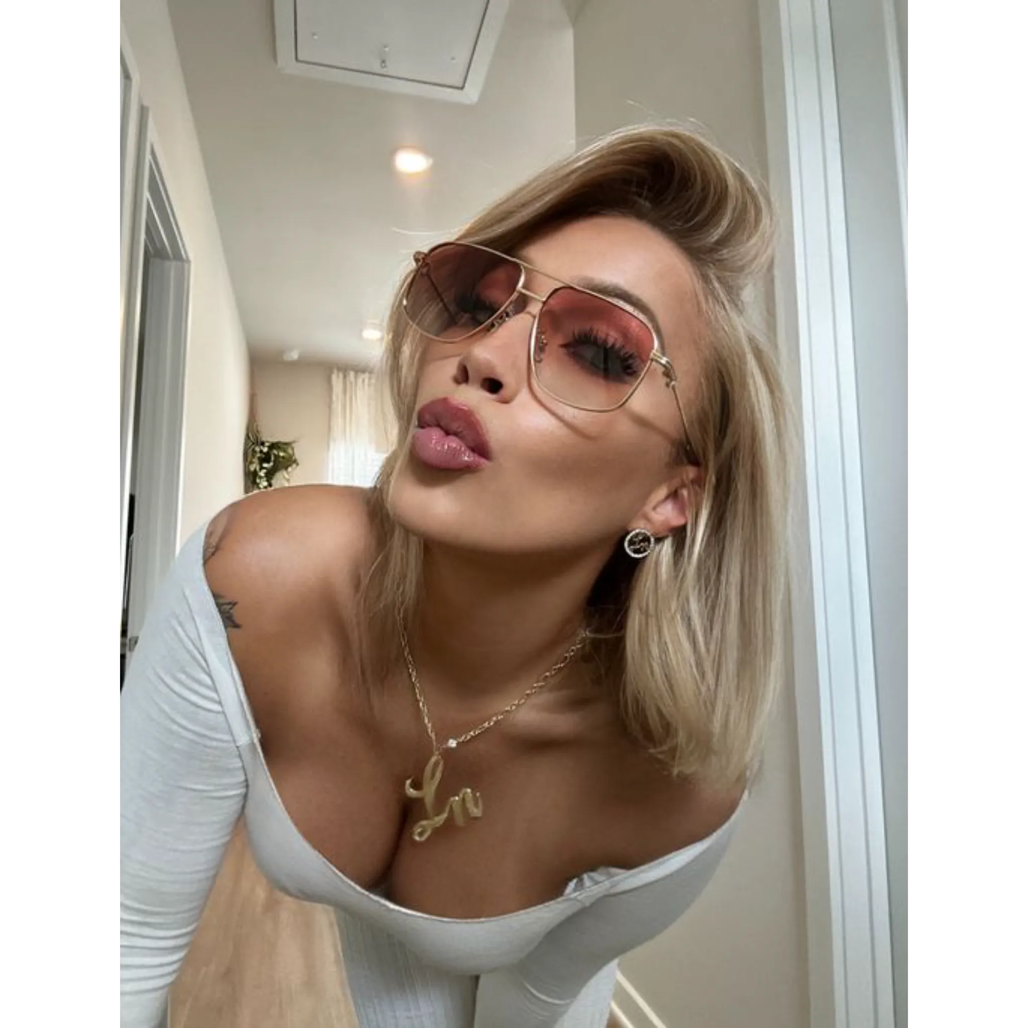 Woman wearing Laurice Noire Lenoah Rose Gold Polarized Sunglasses, posing with a playful kiss in a bright hallway.