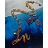 Gold necklace with 'Ln' pendant on a blue textured background