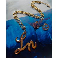 Gold necklace with 'Ln' pendant on a blue textured background