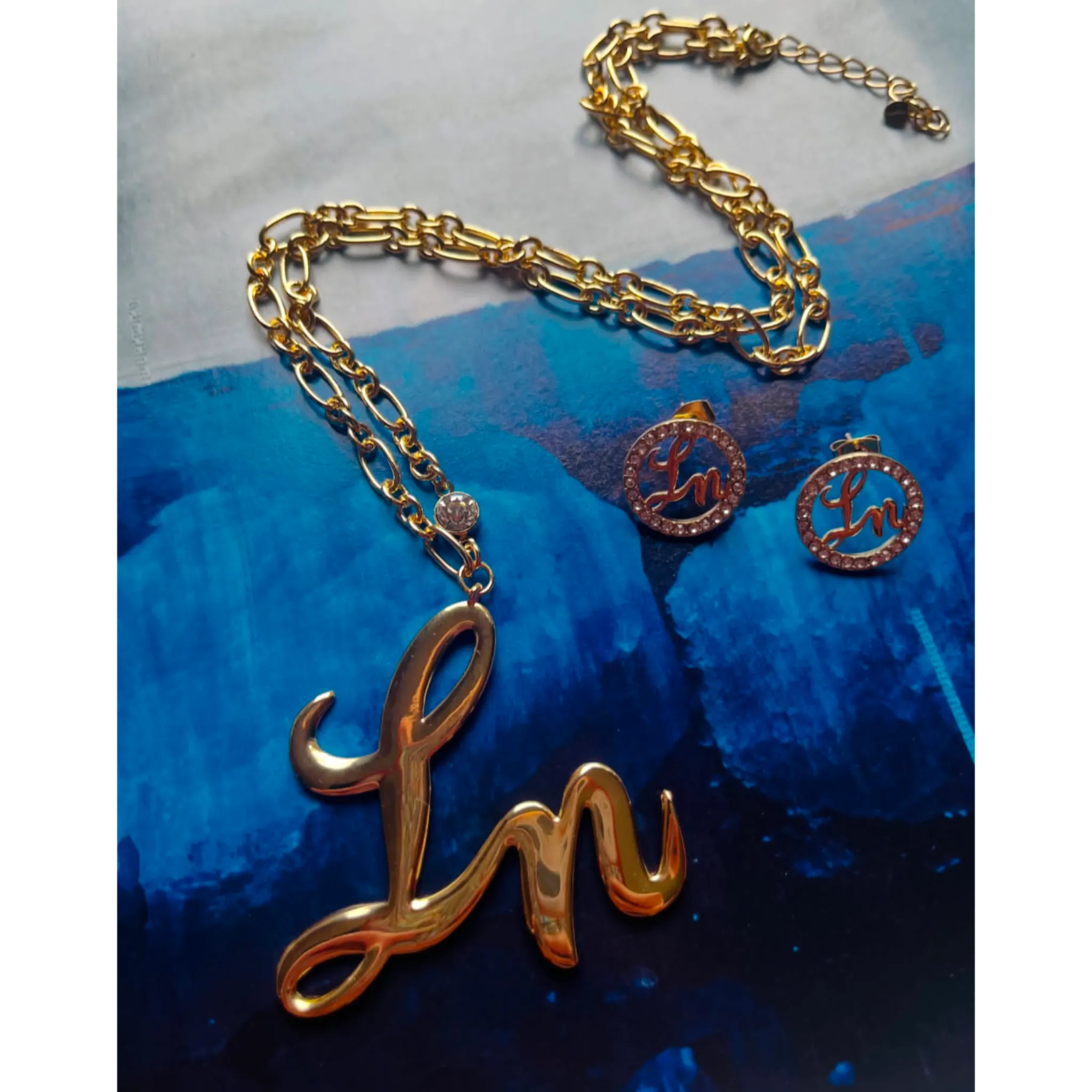 Gold necklace with 'Ln' pendant on a blue textured background