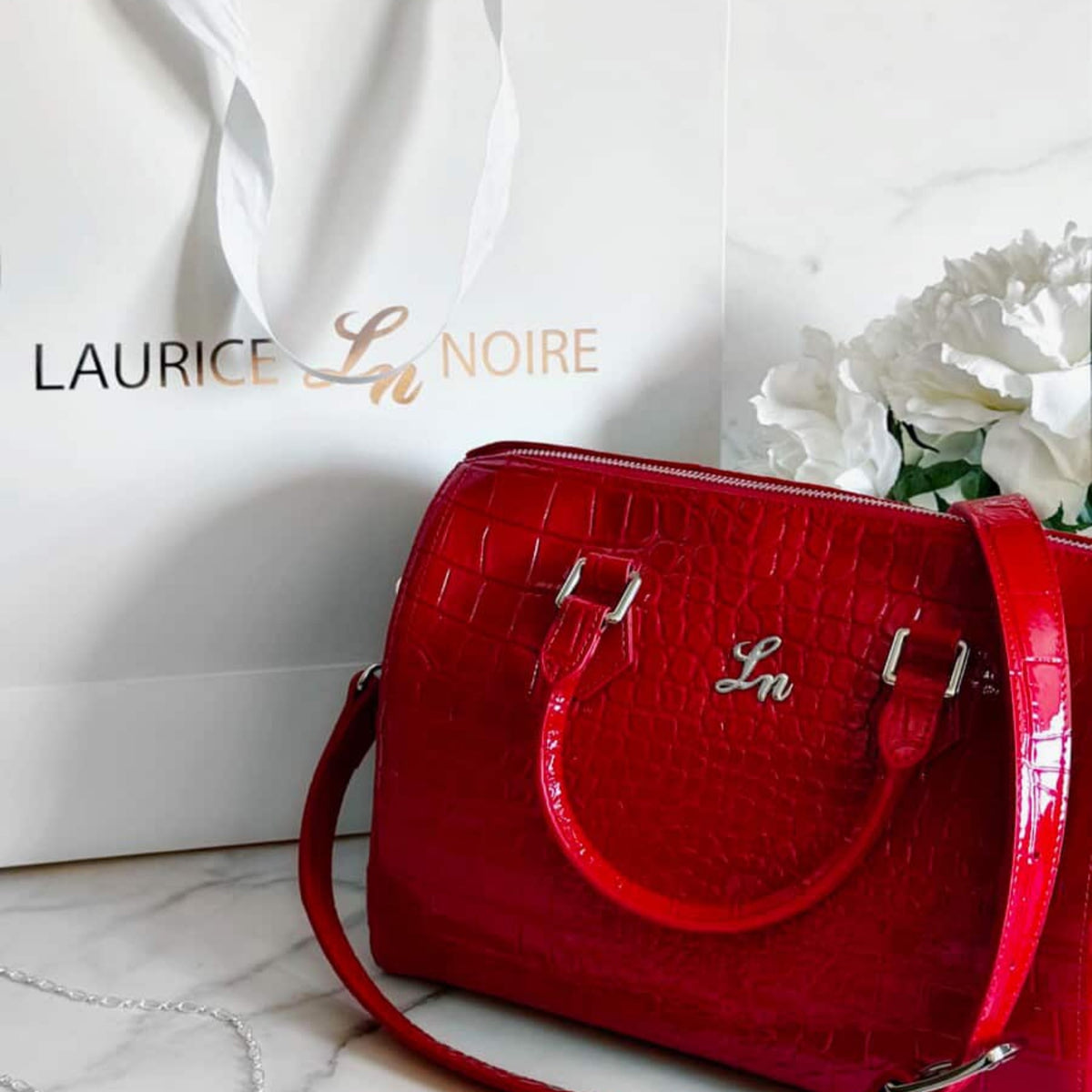 Red handbag with 'Laurice Noire' branding on a white surface.