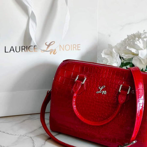 Red handbag with 'Laurice Noire' branding on a white surface.