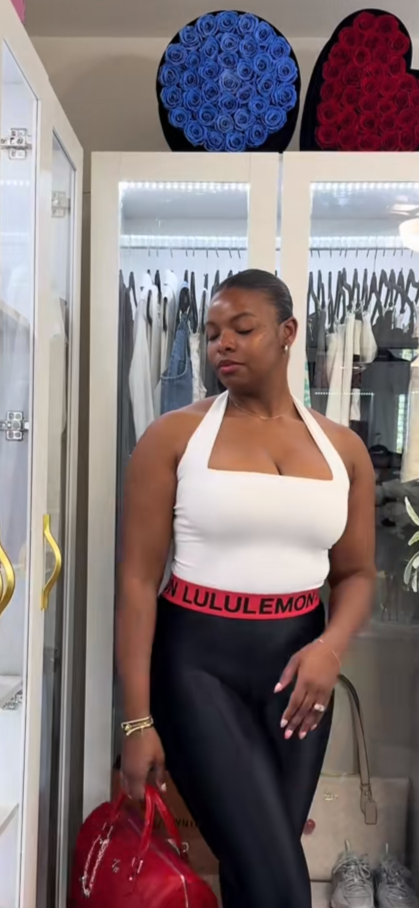 Woman standing in a room with a mirror, holding a red handbag.