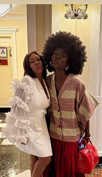 Two women posing together in a hallway with a yellow wall and door.