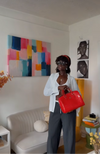 Person holding a red handbag in a room with colorful abstract art and a white couch.