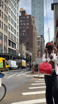 Person with a red handbag crossing a city street with tall buildings in the background