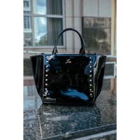 Black patent leather handbag with silver studs on a reflective surface