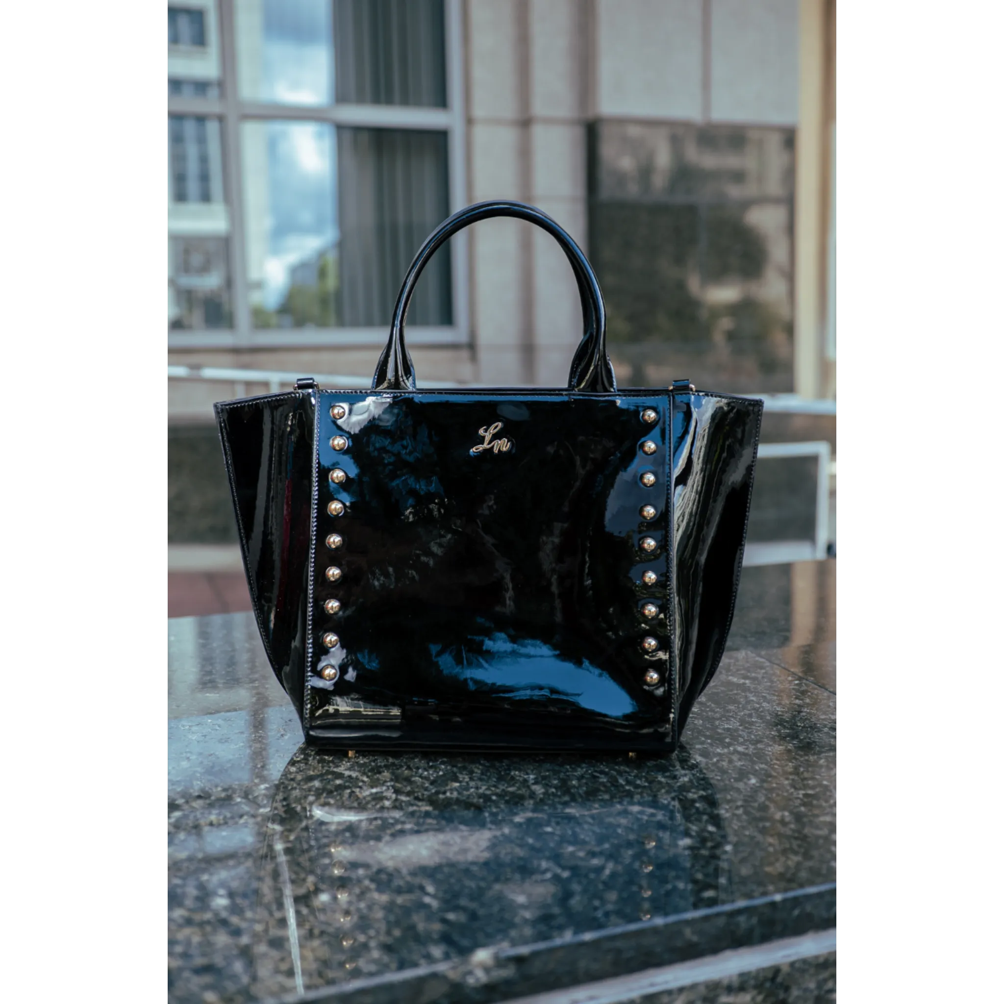 Black patent leather handbag with silver studs on a reflective surface