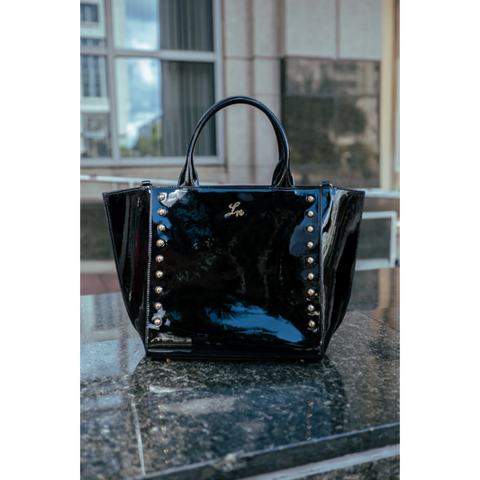 Black patent leather handbag with silver studs on a reflective surface