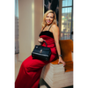 Woman in a red dress holding a black handbag, sitting on a wooden bench.