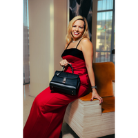 Woman in a red dress holding a black handbag, sitting on a wooden bench.