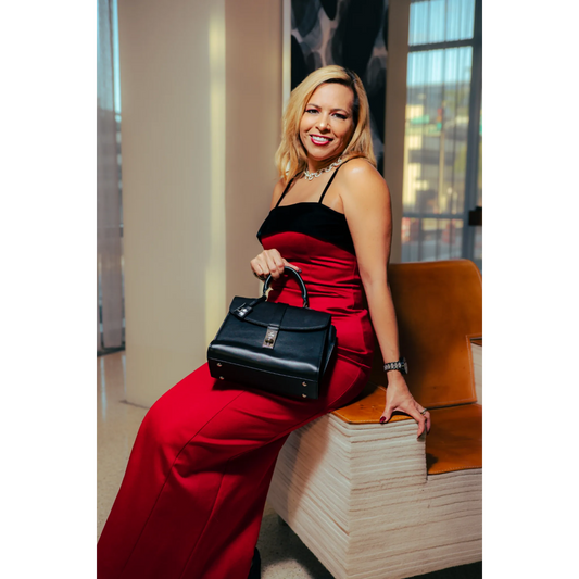 Woman in a red dress holding a black handbag, sitting on a wooden bench.
