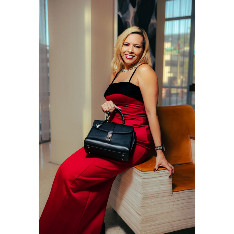 Woman in a red dress holding a black handbag, sitting on a wooden bench.