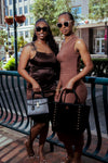 Two women posing outdoors on a city street, wearing sunglasses and holding handbags.