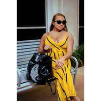 Woman in a yellow and black striped outfit holding a black bag outdoors.