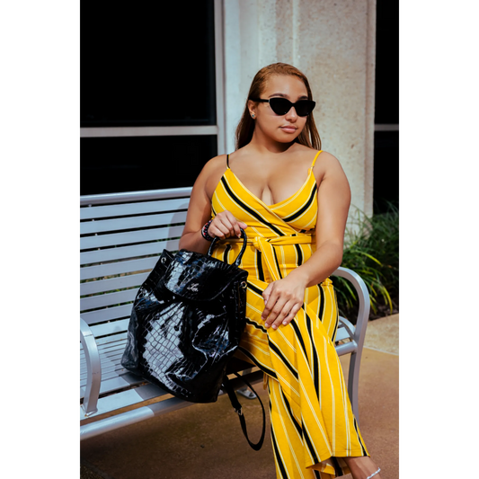 Woman in a yellow and black striped outfit holding a black bag outdoors.