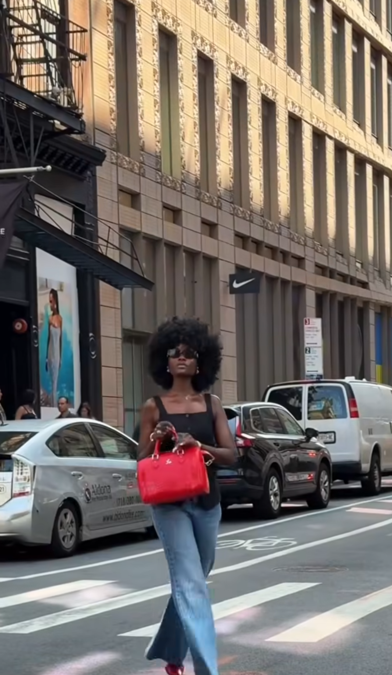 Woman holding a red handbag on a city street with buildings and cars in the background
