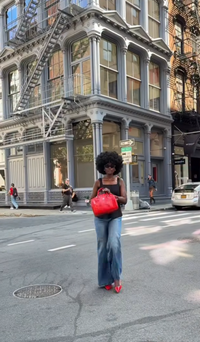 Person with a red bag standing on a city street with buildings and cars in the background